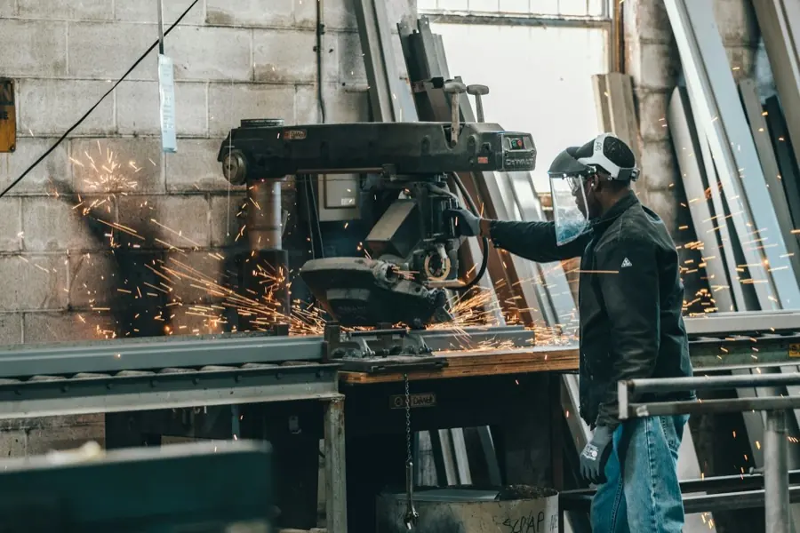 Metallbauer trennt mit der Flex ein Profil, Funkenflug in einer Werkhalle.